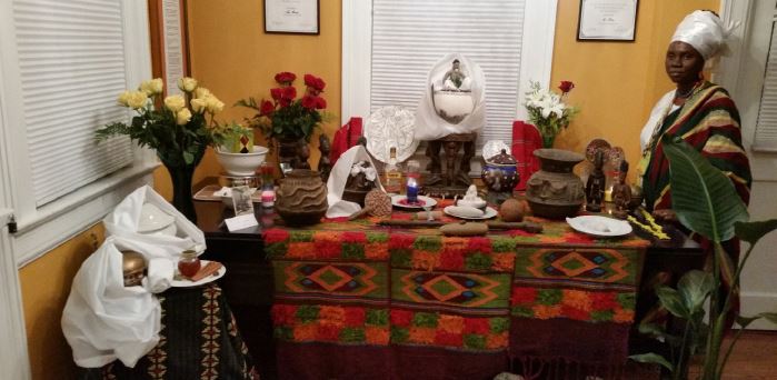 &ndash; &Igrave;y&aacute; Ọ̀ṣun &Ograve; ṣ ogbo, chefe do templo da deusa Ọ̀ṣun na cidade nigeriana de &Ograve;ṣogbo, com minha Yemọja (centro), meus esp&iacute;ritos Ẹgbẹ́ (pote de cer&acirc;mica &agrave; esquerda com o la&ccedil;o e sob pano branco), o altar de minha cabe&ccedil;a (il&eacute; or&iacute;, cilindro forrado de contas no prato fundo &agrave; esquerda); na mesa &agrave; frente, est&atilde;o a Ọ̀ṣun de minha esposa (na bacia de lat&atilde;o &agrave; esquerda) com seu Oxum e Oxal&aacute; (na sopeira branca &agrave; esquerda). Resid&ecirc;ncia do autor, em novembro de 2016 (Durham, NC, Estados Unidos).