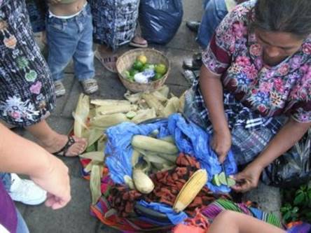 Maya street food vendor selling elotes corn on the cob with lime to Maya handicraft vendors in the Central Plaza