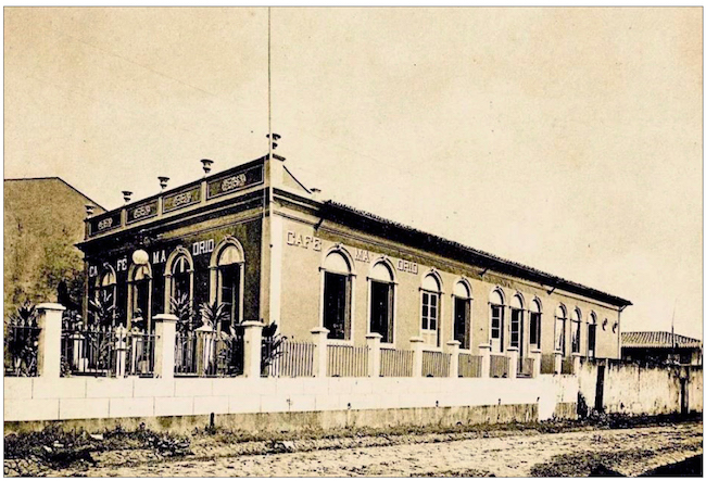 Café Madrid, em frente à Praça da República. Exemplo de edificação em que o uso de platibanda estava apenas na fachada, mantendo o emprego de beirais nas suas laterais. Fonte: Arthur Caccavoni (1899).