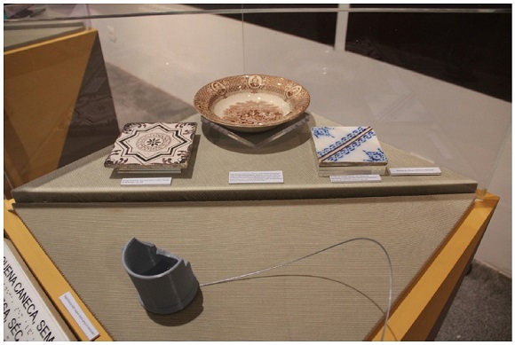 Vitrine com acervo do Museu Hist&oacute;rico Nacional e impress&atilde;o 3D de caneca sem al&ccedil;a. 