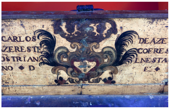 Fotografia com luz UV da arca-cofre RG3242, pertencente ao acervo do Museu Paulista, onde se percebe a incid&ecirc;ncia de pontos de restauro na arca, especialmente em uma faixa vertical ao centro do bras&atilde;o, em tom azulado. H&aacute; tamb&eacute;m pequenos pontos espalhados pela superf&iacute;cie. 