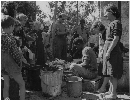 Sentado em um caixote e improvisando uma bancada, o soldado Antônio Martins, de Itatiba (SP), prepara uma grande quantidade de galinhas na cidade italiana de Ponte San Pietro, em setembro de 1944, ajudando a alimentar os civis locais. A felicidade de todos é bastante compreensível, já que a ave vai proporcionar uma refeição quente e fresca, possivelmente com um tempero mais à brasileira, bem diferente dos enlatados norte-americanos.