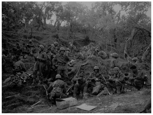 Protegida por uma elevação, uma companhia de fuzileiros da FEB faz uma pausa para a alimentação, com equipamentos e rifles repousando na relva. O caixote de madeira na parte inferior da foto continha a ração tipo C distribuída entre os homens, que dessa vez não tiveram o luxo de receber uma refeição quente: todos eles comem direto das latas.