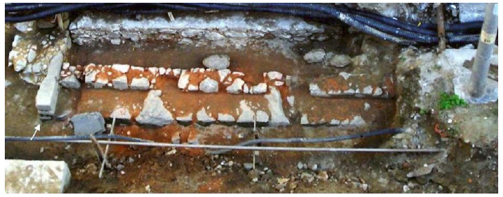 Os alicerces de alvenaria de pedra do trapiche 1, em frente ao atual n&ordm; 40 da Rua Coelho e Castro. &Agrave; esquerda, a seta aponta um elemento de for&ccedil;a engastado na parede, provavelmente para maquin&aacute;rio destinado a i&ccedil;ar cargas, seguido, na extrema esquerda, de um piso refor&ccedil;ado com a frente arredondada. Foto: Studio Soma.