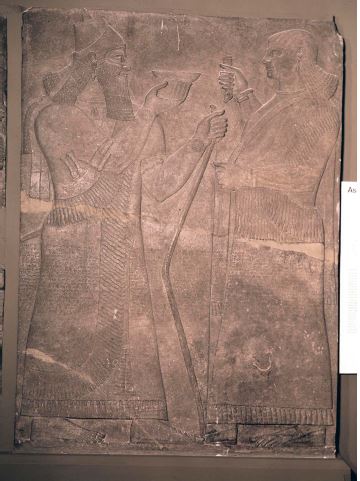 “Gypsum wall panel relief: showing a formal scene. Ashurnasirpal II appears holding a bow and bowl flanked by a human attendant with a fly-flapper”. Production date: 865-860 BCE”.