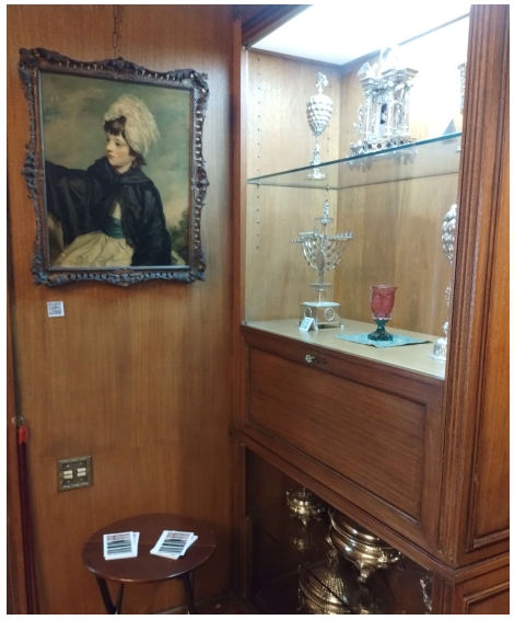 Recursos expogr�ficos textuais dispon�veis na CMEK. Um cart�o com texto e imagem, exposto em cima de um banco para o p�blico pegar e um QR Code, fixo na parede embaixo da pintura.