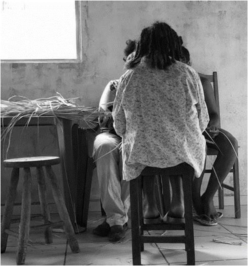 Crianças e moradora mais velha da comunidade executando atividade artesanal com palha de licuri.