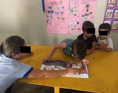 Gustavo e a professora leem o livro “Mãenhê!” ao lado de dois colegas de sala