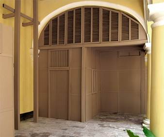 Casa de la Obra Pía. Instalación en cartón corrugado de casa encajada dentro de un arco de puntal alto. La vivienda ocupa el área de acceso a la antigua cochera del inmueble, 400 x 400 cm aprox.