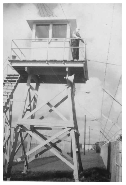 Patio de recreo en el PIDC, aprox. 1981. Debido al intenso calor en el RGV, el INS proporcionó un área de sobra para los detenidos en el patio de recreo detrás del original Centro de Detención de Port Isabel. Cerca de una docena de toldos más pequeños eventualmente quedaron desperdigados por la propiedad. Los agentes de detención vigilaban a los detenidos en el patio desde su torre de observación. PM (Fotografía 11.206f, aprox. 1981, n.d., p.206; Fotografía 11.206i, aprox . 1981, n.d.; Fotografía 11.206j, aprox. 1981, n.d.).