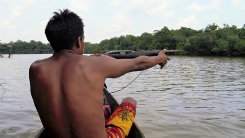 Kier&atilde;sa, balancing in a canoe, aims his shotgun towards prey on the shores of K&ocirc;tunsi Lake