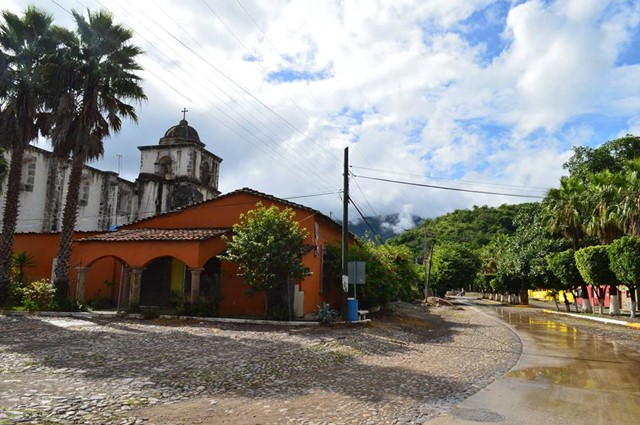 Capilla y tienda de raya, edificio reconstruido, de la ex hacienda de Ayacapán en el valle de Autlán-El Grullo, seleccionado por su topografía: varias elevaciones, Sierra de Cacoma y Sierra de Manantlán al norte, oeste y sur, además del cerro Las Joyas de los Zapotes. Se aprecia también un arroyo que sólo en temporada de lluvia muestra alguna corriente. Archivo de campo, 23 de septiembre de 2017.