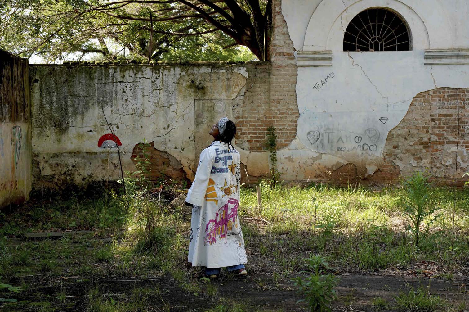 &Aacute;rea externa da Oficina de Criatividade do HPSP,2019. Solange veste obra que homenageiaos cinco participantes de Epidemia de Coresque haviam falecido desde sua realiza&ccedil;&atilde;o,produzindo interlocu&ccedil;&atilde;o com a obraaudiovisual e com o coletivo de participantesda Oficina de Criatividade. Ao fundo, galhos da&Aacute;rvore de Galli.