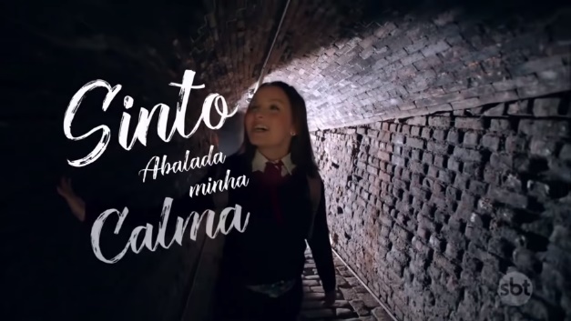 Mirela e Raquel cantam em um túnel, acompanhadas pela letra da canção