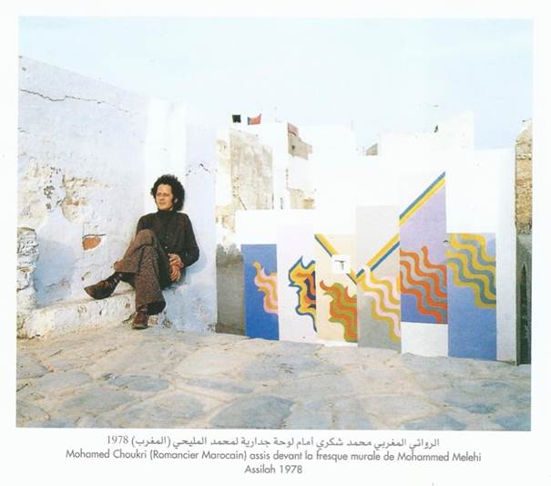 Mohamed Choukri sitting in front of a mural by Mohamed Melehi, Asilah 1978. Image reproduced from the book Peinture murale d’Asilah. vasions dans l’imaginaire by the Fondation du Forum d’Asilah, p. 28.