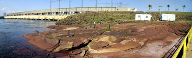 The geosite: aeolian sandstones outcrop of the Rio Paraná Formation where the tracks occur is on the right. The concrete structure of the dam of the Porto Primavera Hydroelectric Plant is in the background.