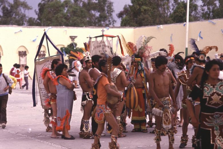 Dancers at Los Remedios during a break in the dance and wearing Aztec
                            style costumes: A mesa of gente humilde with probably
                            scarce resources judging by the simplicity of their headdresses
                            (1989).