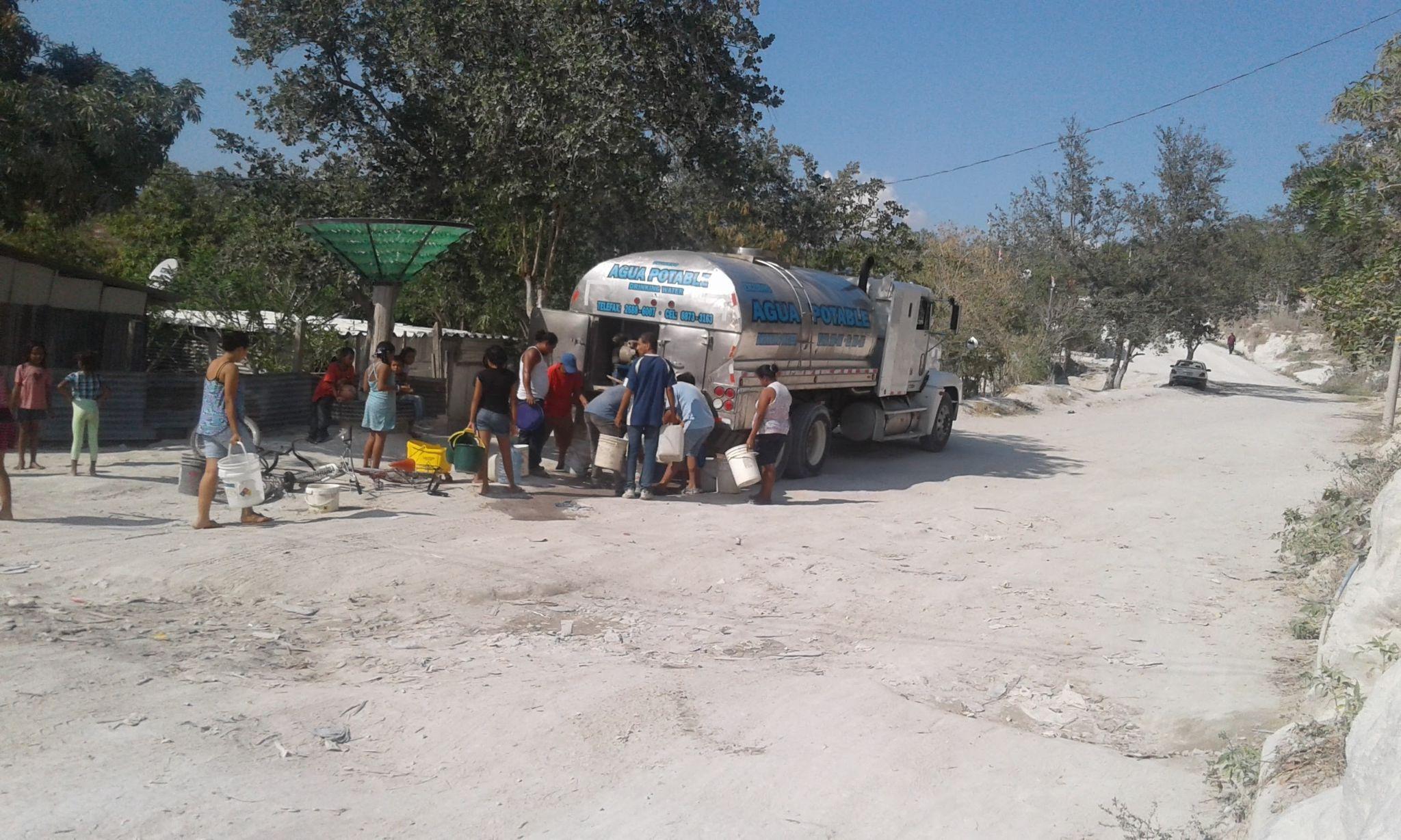 Distribuci�n de agua potable en la comunidad de Martina Bustos. La fotograf�a muestra a habitantes de la comunidad recolectando agua suministrada por un cami�n cisterna debido a los cortes del servicio en los tubos comunales. El cami�n est� estacionado justo enfrente de un tubo comunal que no es visible en la imagen, ya que queda cubierto por el veh�culo.